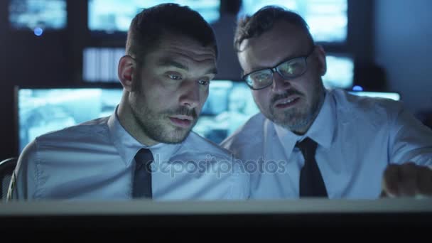 Två anställda har en konversation bredvid en dator i ett mörkt övervakning rum fyllda med skärmar. — Stockvideo
