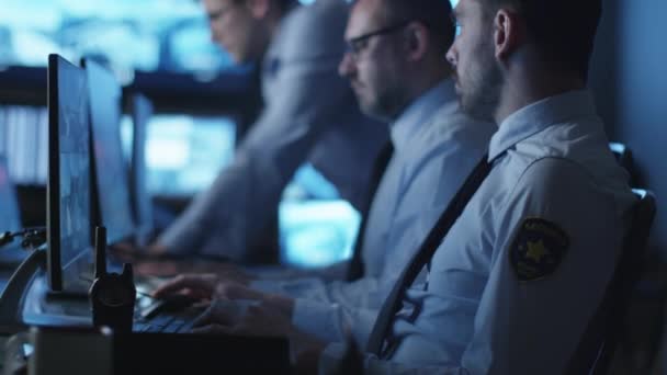 Groupe d'agents de sécurité travaillent dans une salle de surveillance sombre remplie d'écrans d'affichage .