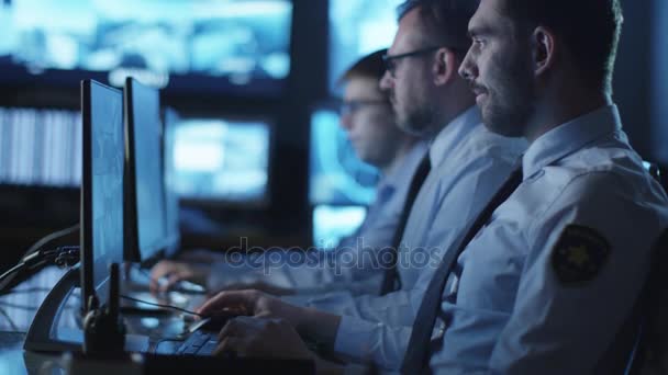 Groupe d'agents de sécurité travaillent dans une salle de surveillance sombre remplie d'écrans d'affichage .