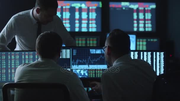 Team of stockbrokers are having a conversation in a dark office with display screens. — Stock Video