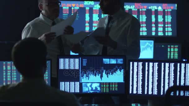 Dois corretores de bolsa estão tendo uma discussão no trabalho em um escritório escuro com telas de exibição . — Vídeo de Stock