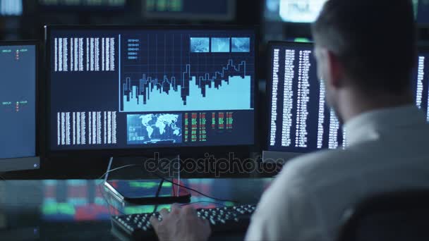 El hombre está trabajando en una computadora con datos y gráficos en una oficina oscura llena de pantallas . — Vídeo de stock