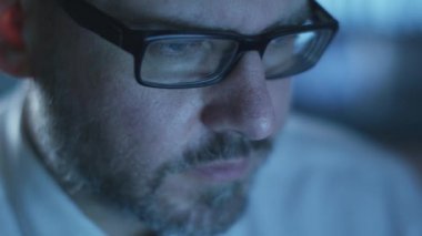 Yöneticisi bir bilgisayarda göstermek perde ile dolu bir karanlık office odada akşam çalışıyor.