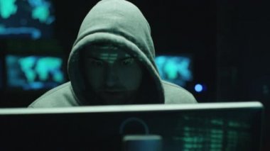 Yeşil kod karakterleri karanlık bir ofiste yüzünü yansıtırken, erkek hacker bilgisayar üzerinde çalışıyor..