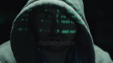 Yeşil kod karakterleri karanlık bir ofiste yüzünü yansıtırken, erkek hacker bilgisayar üzerinde çalışıyor..