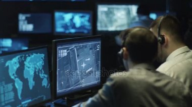 İki BT uzmanları işadamı uydudan dolu karanlık bir izleme odada bilgisayarda üzerinden casusluk görüntüleme ekranları.