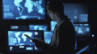 Gözlüklü adam karanlık bir izleme odada göstermek perde ile dolu bir tablet bilgisayar kullanıyor.