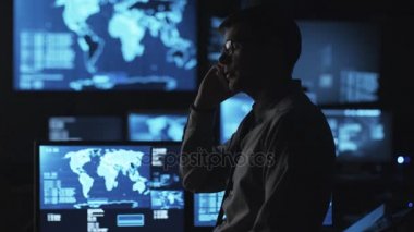 Gözlüklü adam göstermek perde ile dolu karanlık bir izleme odada telefonda konuşuyor.