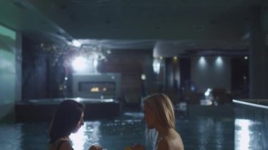 İki genç çekici kadın havuzu oturan ve bir spa Sağlık Merkezi konuşuyor.