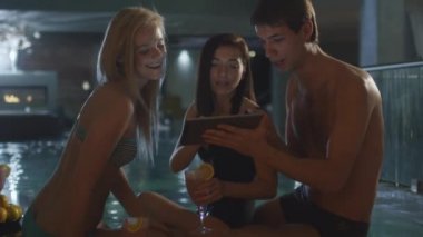Arkadaş grubu bir spa Sağlık Merkezi bir havuzda yakınındaki bir tablet bilgisayar kullanırken eğlenceli yaşıyorsanız.
