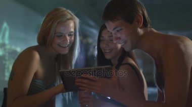 Arkadaş grubu bir spa Sağlık Merkezi bir havuzda yakınındaki bir tablet bilgisayar kullanırken eğlenceli yaşıyorsanız.