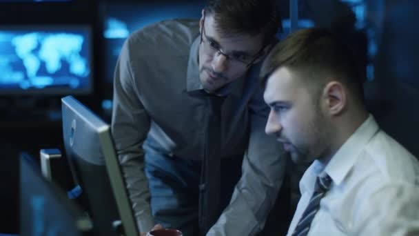 Deux programmeurs informatiques travaillent sur ordinateur dans une salle de bureau sombre remplie d'écrans d'affichage .