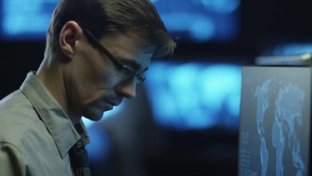 Programador profesional de TI en gafas está trabajando en la computadora en la habitación oscura de la oficina llena de pantallas de visualización . — Vídeos de Stock