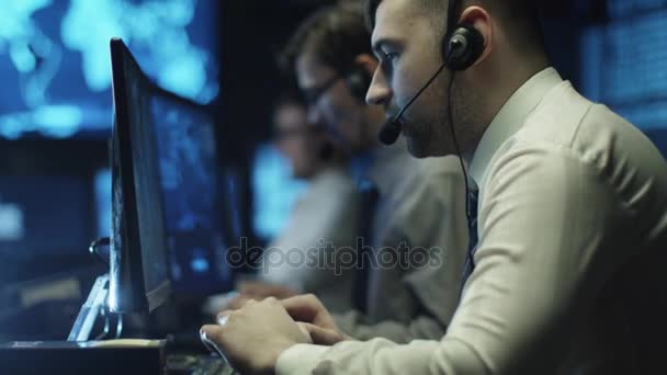 Deux programmeurs informatiques travaillent sur ordinateur dans un casque dans une salle de bureau sombre remplie d'écrans d'affichage .