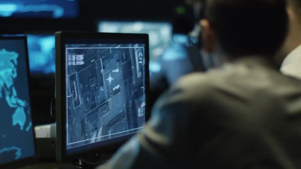 Deux professionnels de l'informatique espionnent un homme d'affaires grâce à une surveillance par satellite sur ordinateur dans une salle de surveillance sombre remplie d'écrans d'affichage . — Video