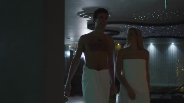 若い男性と女性がスパ ウェルネス センターでタオルでプールサイドに沿って歩いています。. — ストック動画