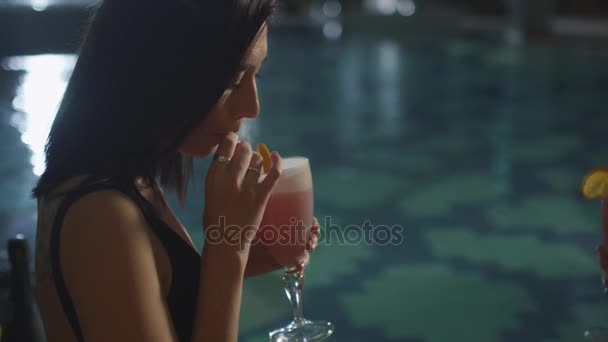 Fiatal, vonzó nő ül a medence mellett, és iszik egy koktélt a szalma, a spa wellness központ. — Stock videók