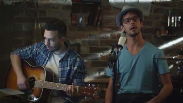 Due giovani cantano e suonano la chitarra mentre registrano una canzone in uno studio casalingo in un garage . — Video Stock