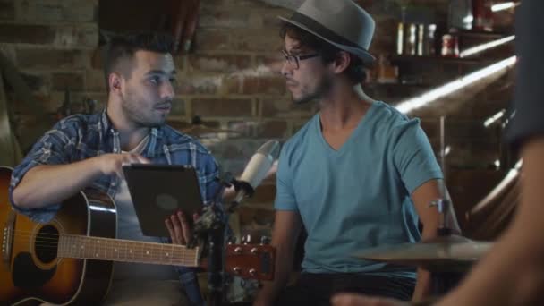 Band av musiker har en diskussion i ett garage studio medan du använder en tablet PC. — Stockvideo