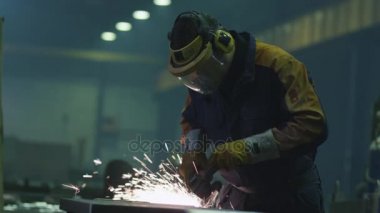 Sıcak sparks bir sonucunda üretilen ağır sanayi işçisi bir fabrikada metal ile açı değirmeni üzerinde çalışıyor.