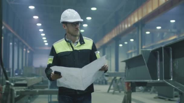 Ingeniero en hardhat se está moviendo a través de una fábrica de la industria pesada con un plano . — Vídeo de stock