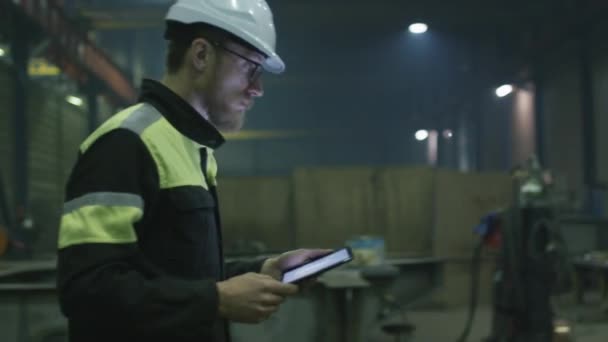 Ingénieur en hardhat se déplace à travers une usine de l'industrie lourde avec un ordinateur tablette .