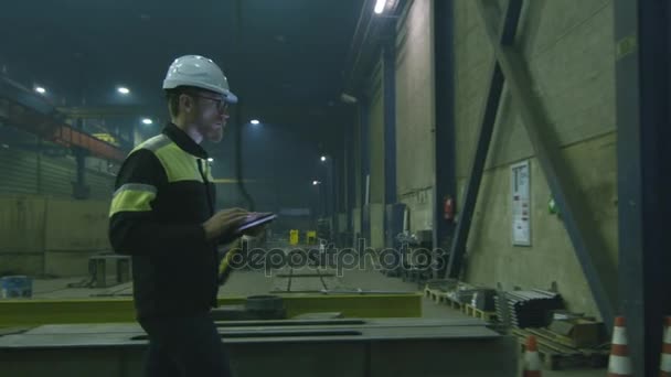 Μηχανικός στο hardhat κινείται μέσα από ένα εργοστάσιο της βαριάς βιομηχανίας με έναν υπολογιστή tablet. — Αρχείο Βίντεο