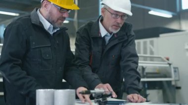 Bir fabrikada bir tablet bilgisayardaki bilgileri denetlenirken bir plan iki mühendis tartışmak.