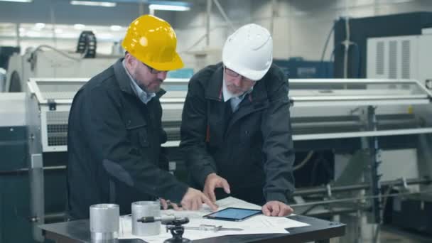 Twee ingenieurs bespreken een blauwdruk terwijl het controleren van de informatie op een tablet-pc in een fabriek. — Stockvideo