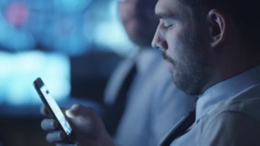 Karanlık bir izleme odada çalışma göstermek perde ile dolu iken güvenlik görevlisi smartphone cep telefonu ile sosyal medya kontrol ediyor.