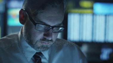 Yöneticisi bir bilgisayarda göstermek perde ile dolu bir karanlık office odada akşam çalışıyor.