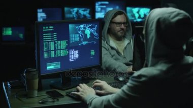 Haritalar ile bir bilgisayarlarda davlumbaz çalışır ve veri göstermek perde bir karanlık office odada üzerinde iki bilgisayar korsanları.