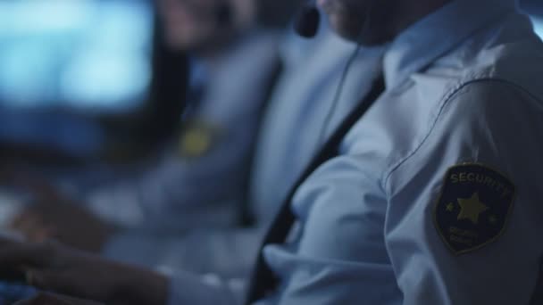 Agent de sécurité parle sur un casque tout en travaillant sur un ordinateur dans une salle de surveillance sombre remplie d'écrans d'affichage .