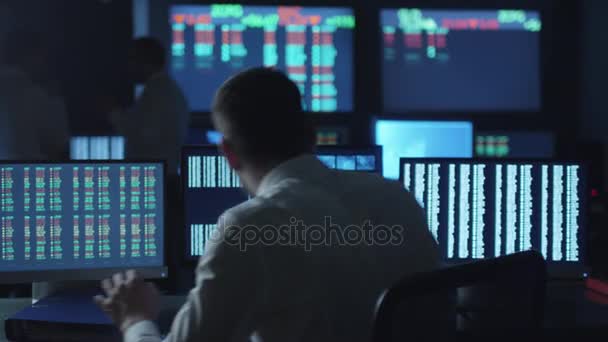 Börsmäklare i vit skjorta arbetar i ett mörkt övervakning rum med skärmar. — Stockvideo