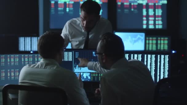 Team of stockbrokers are having a conversation in a dark office with display screens. — Stock Video