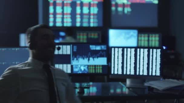 Feliz corretor de bolsa de sucesso está torcendo em uma cadeira que trabalha em uma sala de monitoramento escuro com telas de exibição . — Vídeo de Stock