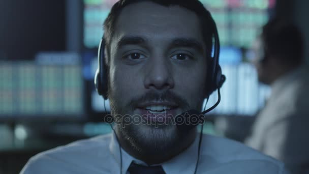 L'employé du soutien à la clientèle parle sur un casque pendant qu'il travaille sur un ordinateur dans un bureau sombre rempli d'écrans d'affichage .
