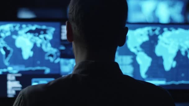 Manlig anställd övervakar kartor och data på dator skärmar i en mörk kontorsrum. — Stockvideo