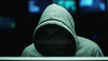 Erkek hacker yüzünü ışık karanlık office odasında gizli olmasını bir başlık giyen bir bilgisayarda çalışma.