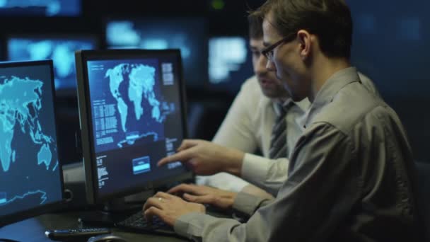 Twee het programmeurs werken op computer in een donkere office kamer gevuld met schermen. — Stockvideo