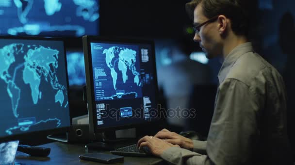 Programador profesional de TI en gafas está trabajando en la computadora en el centro de seguridad cibernética lleno de pantallas . — Vídeos de Stock