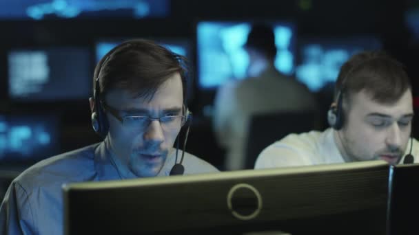 Une équipe de professionnels de l'informatique travaille sur un ordinateur dans une pièce sombre remplie d'écrans d'affichage .