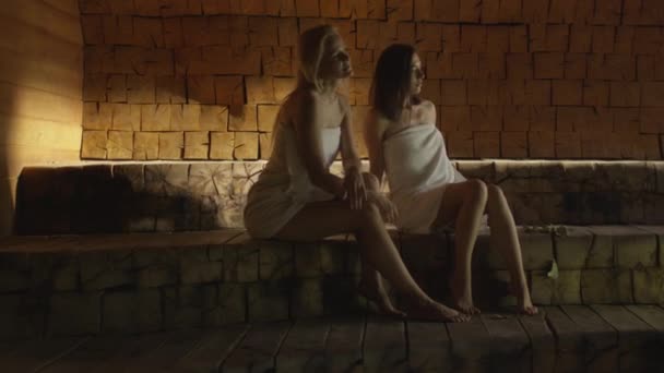 Zwei attraktive Mädchen in Handtüchern entspannen sich in einem Dampfbad im Wellness-Zentrum. — Stockvideo