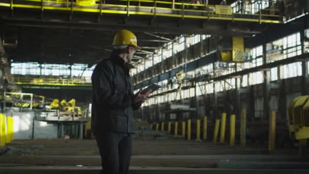 Techniker in harter Mütze im industriellen Umfeld. Tablet in den Händen halten. — Stockvideo