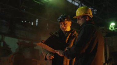 Mühendis ve işçi döküm içinde görüşme. Zorlu endüstriyel ortamlar. Orta atış.