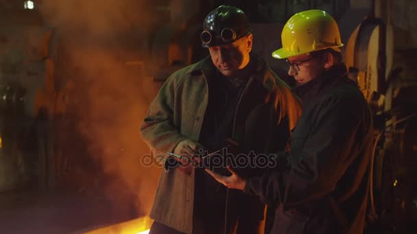 Inženýr a zaměstnance vést konverzaci ve slévárně. Inženýr, pomocí Tablet. Drsné průmyslové prostředí. — Stock video