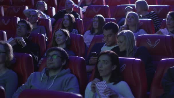 El hombre está usando su teléfono inteligente mientras la gente está viendo una proyección de cine en un cine . — Vídeos de Stock