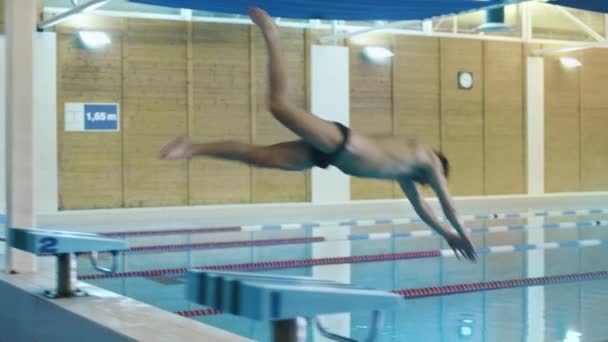 Profi-Schwimmer springt aus dem Startblock und führt den Schmetterlingsschlag aus. Kamera folgt ihm. — Stockvideo