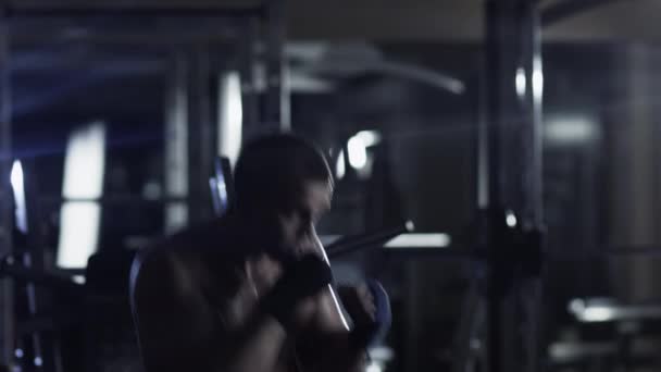 Boxeador masculino profesional está entrenando golpes y patadas en el gimnasio oscuro . — Vídeo de stock