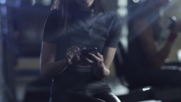 Atractiva chica deportiva en forma está utilizando su teléfono inteligente en el gimnasio . — Vídeos de Stock